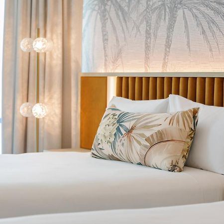 아모라 브리즈번 호텔 외부 사진 The photo shows a stylish hotel room featuring two neatly made beds with white linens. Each bed has several pillows, one of which has a decorative cover with a tropical plant pattern. Behind the beds is a modern headboard, and the wall is decorated w