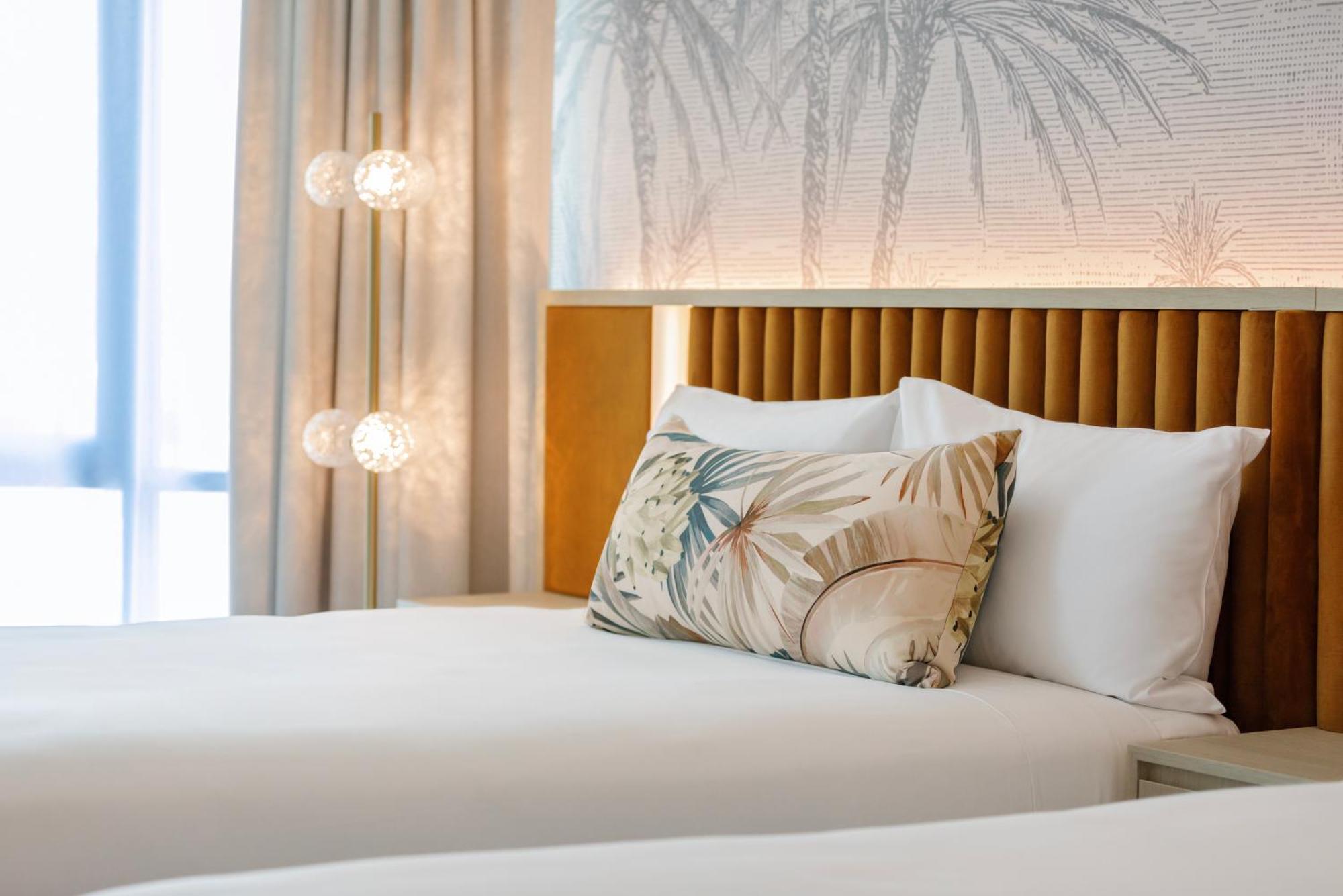 아모라 브리즈번 호텔 외부 사진 The photo shows a stylish hotel room featuring two neatly made beds with white linens. Each bed has several pillows, one of which has a decorative cover with a tropical plant pattern. Behind the beds is a modern headboard, and the wall is decorated w